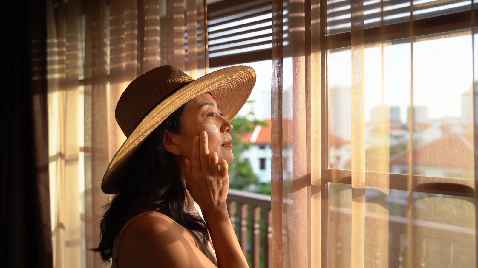 An East Asian woman in her late 30s wearing a wide-brimmed straw hat in dappled sunlight on a Singapore terrace — illustrative image
