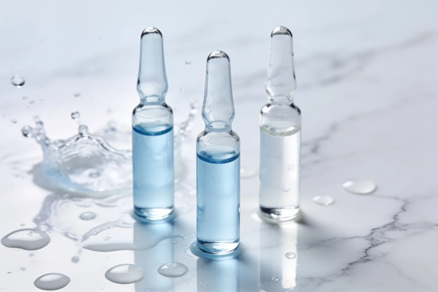 Three small glass ampoules of clear and pale-blue hydrating solution on white marble